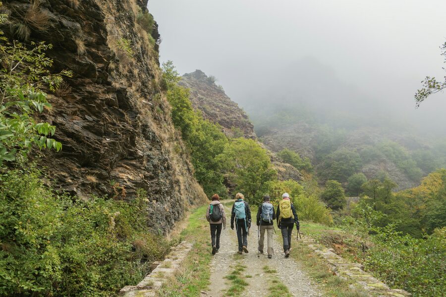 Cuatro personas caminando por un sendero de tierra entre montañas